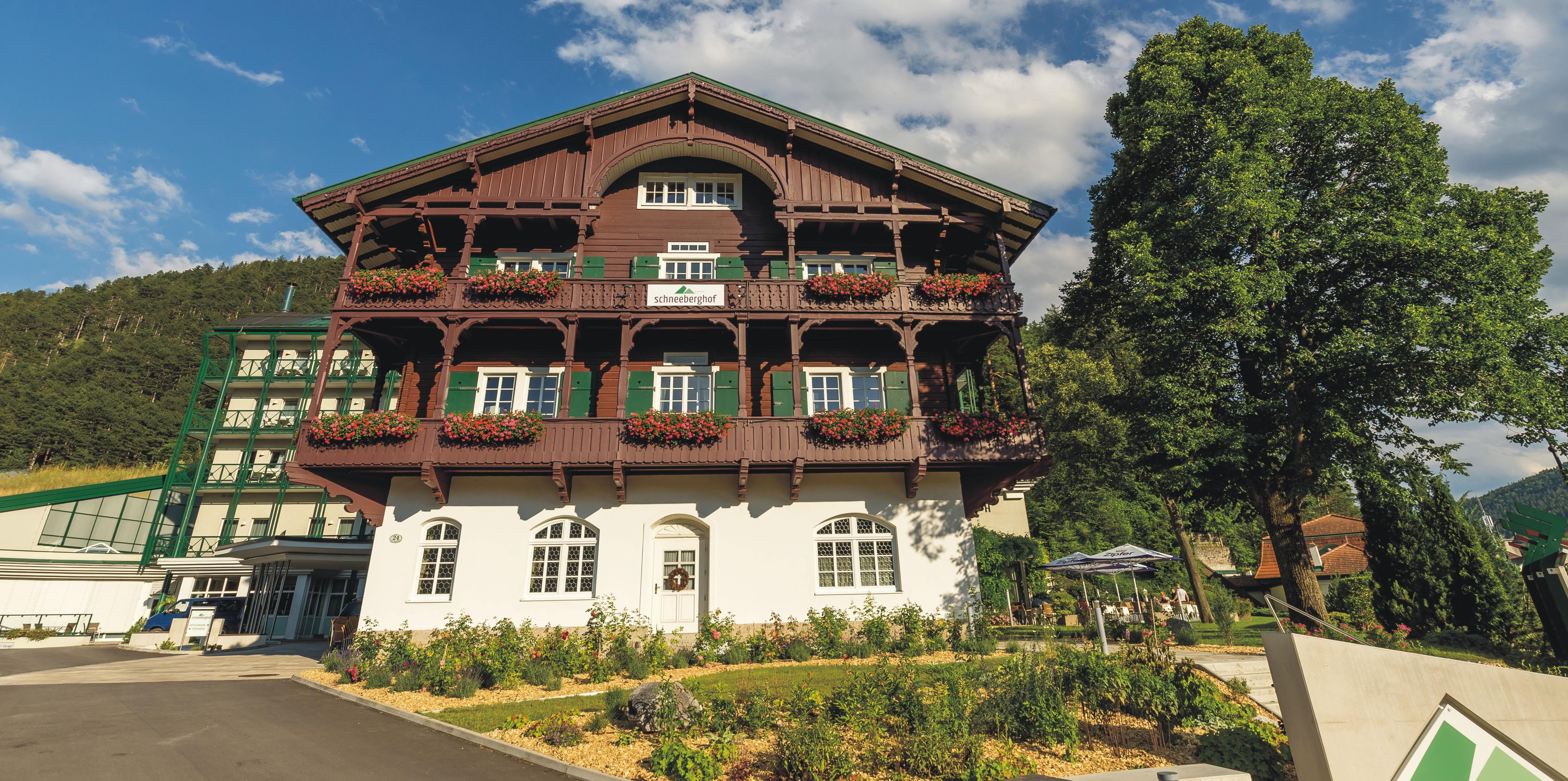 Hotel Schneeberghof mit Blumen geschmücktem Balkon und blauen Himmel.