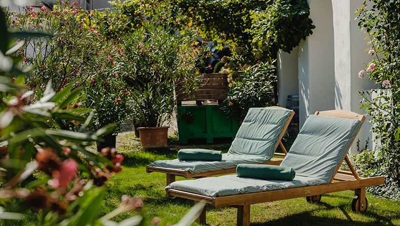 Zwei Liegestühle im grünen Garten mit Pflanzen und Blumen.
