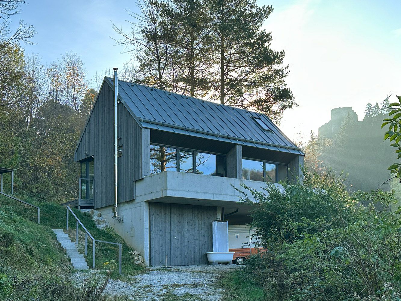 Modernes Haus mit Holzfassade und großen Fenstern in bewaldeter Umgebung.