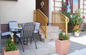 Eingangsbereich einer Ferienwohnung mit Terrasse, Tisch und Stühlen, Blumen und Geländer.