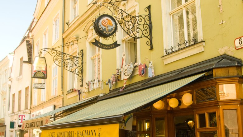 Au&szlig;enansicht der Konditorei Hagmann mit gelbem Vordach und Stra&szlig;encaf&eacute;.