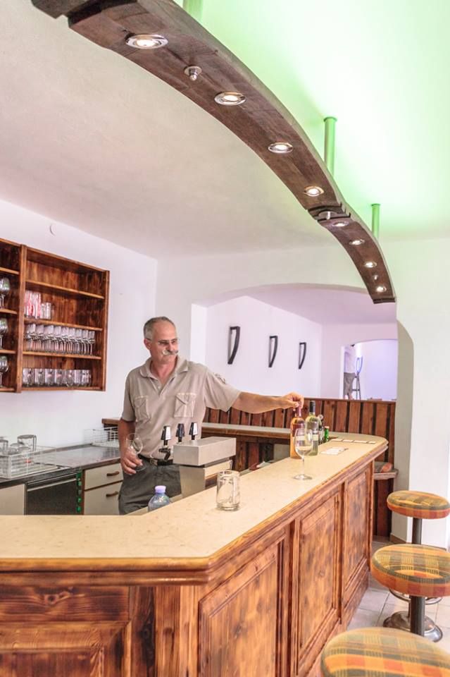 Ein Mann steht hinter einer Holzbar in einem Weinkeller und schenkt Wein ein.