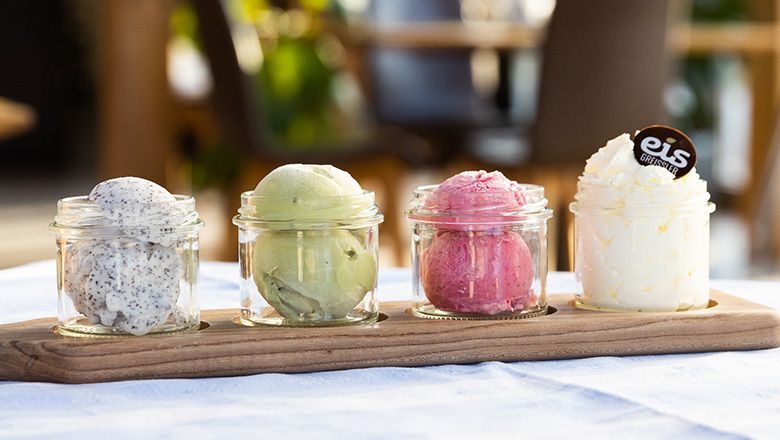 Vier Gläser mit verschiedenen Eissorten auf einem Holzbrett.