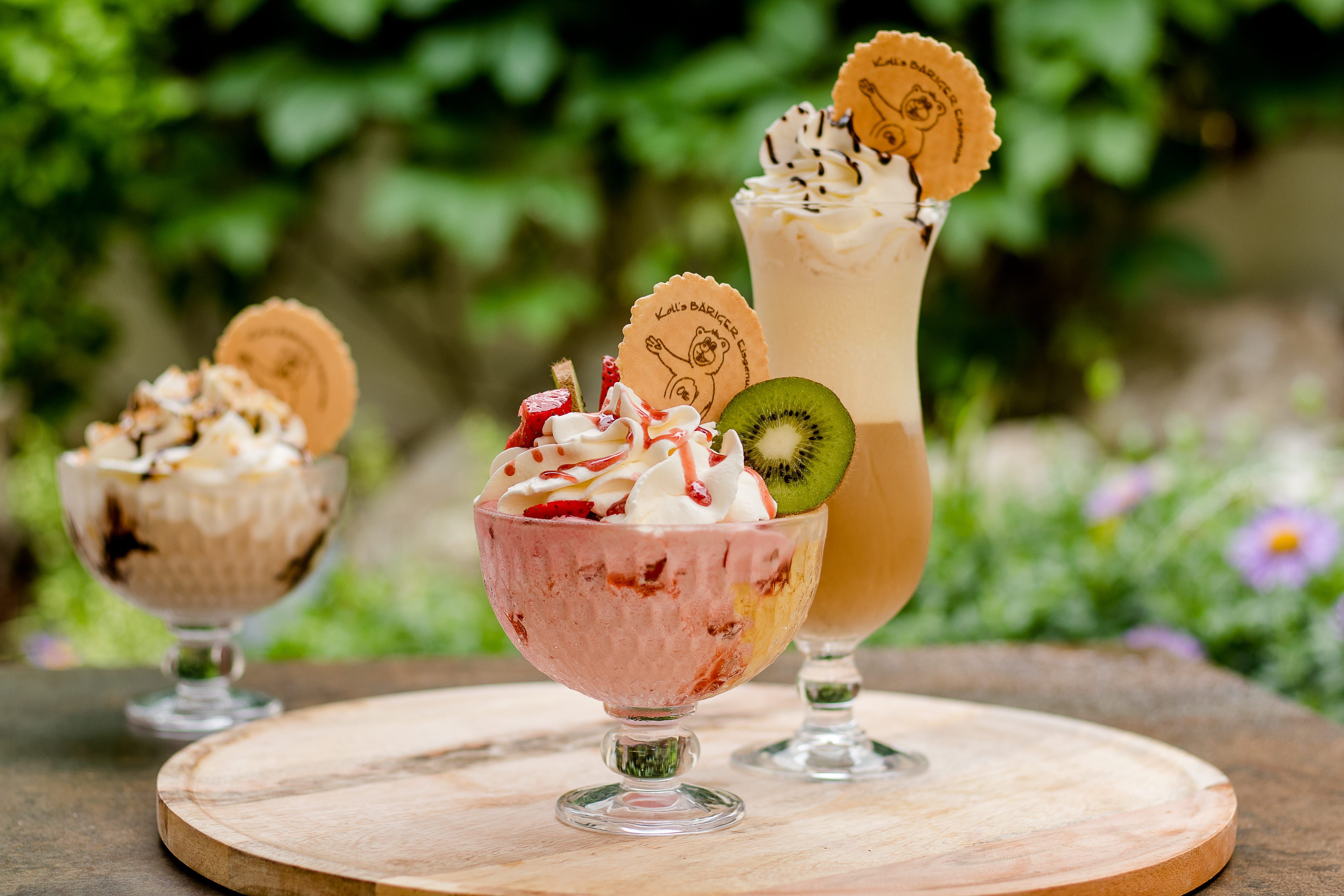 Drei Eisbecher und ein Eiskaffee auf einem Holztisch im Freien.