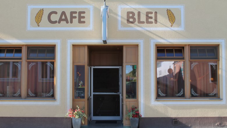 Eingang eines Cafés mit der Aufschrift 'Cafe Blei' und Blumendekoration.