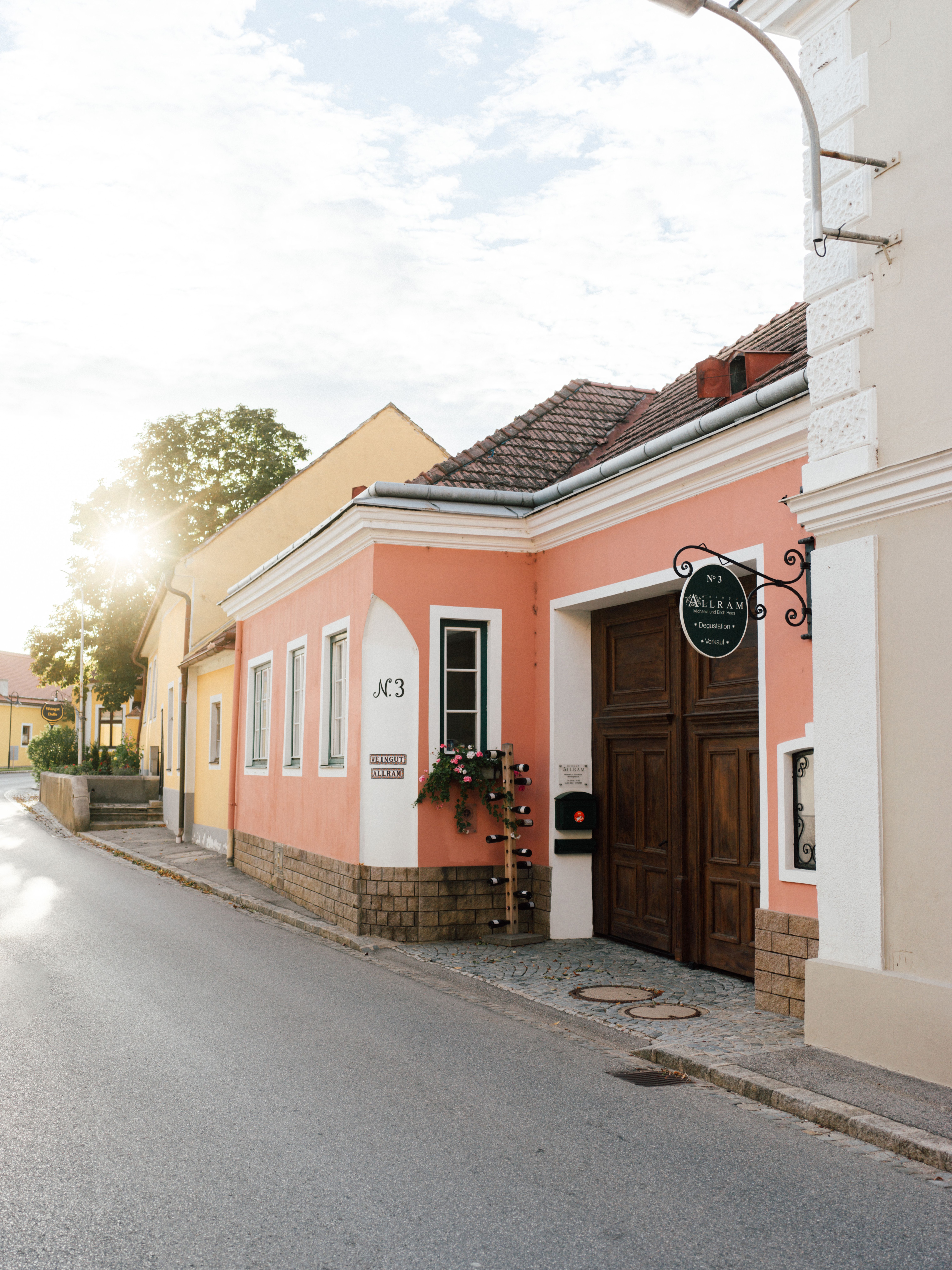 In der sanften Morgenröte erstrahlt das Weingut Allram in warmen Farben und lädt zu einem genussvollen Aufenthalt ein. Die blühenden Pflanzen und die charmante Architektur schaffen eine einladende Atmosphäre, die zum Verweilen einlädt. Hier, umgeben von malerischen Weinbergen, erleben Besucher die Schönheit der Natur und die Tradition des Weinbaus.