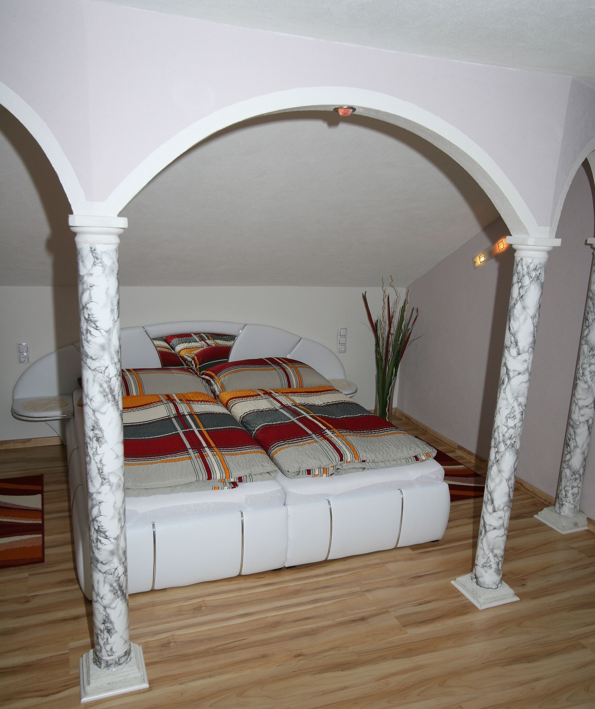 Schlafzimmer mit Doppelbett, Marmorsäulen und gestreifter Bettwäsche.