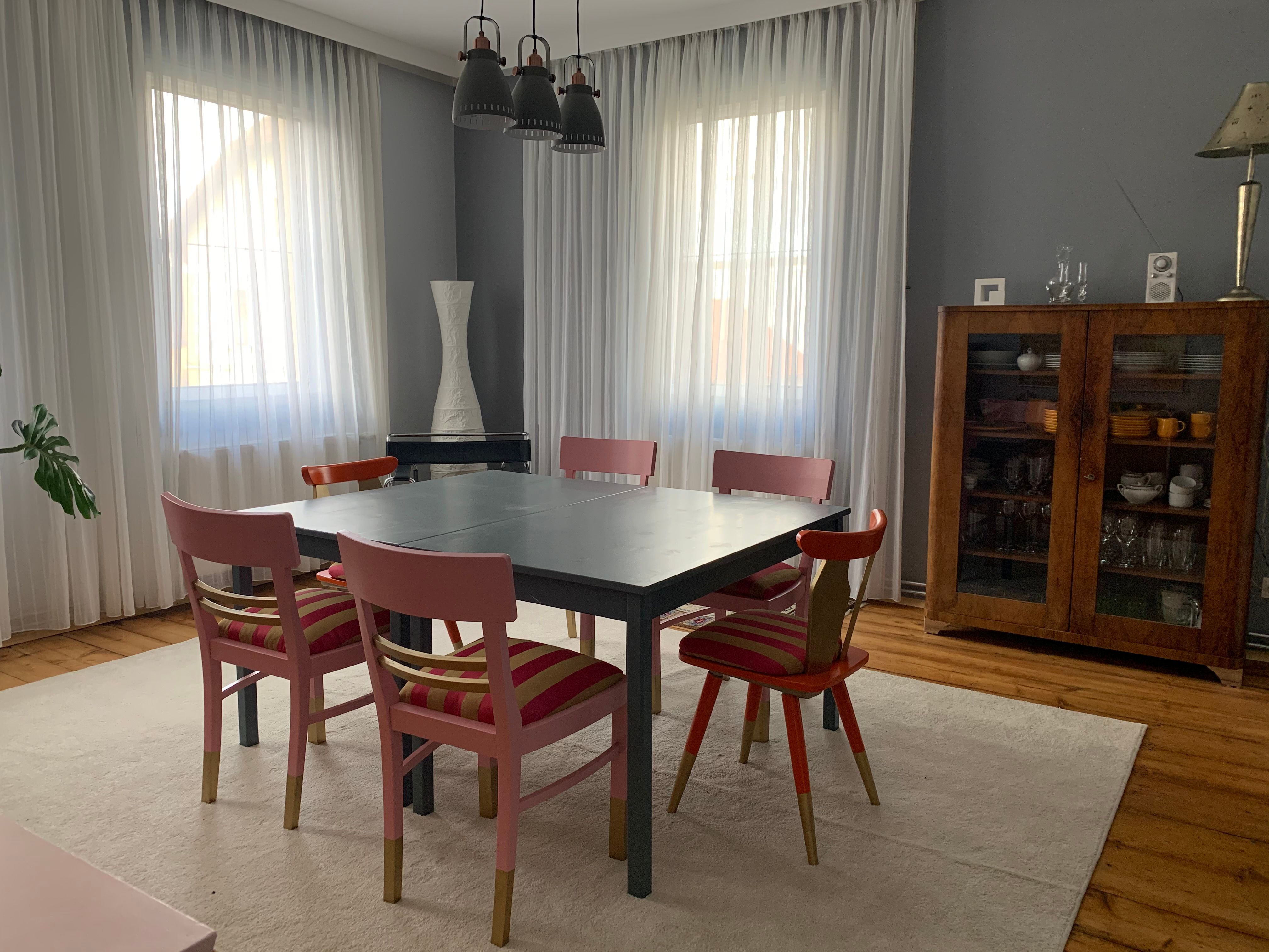 Esszimmer mit Tisch, sechs Stühlen, Vitrine und Vorhängen.