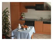 Appartement, © © Fam Pekarek Kleine Küche mit Holzmöbeln, Esstisch mit blauer Tischdecke und Geschirr.