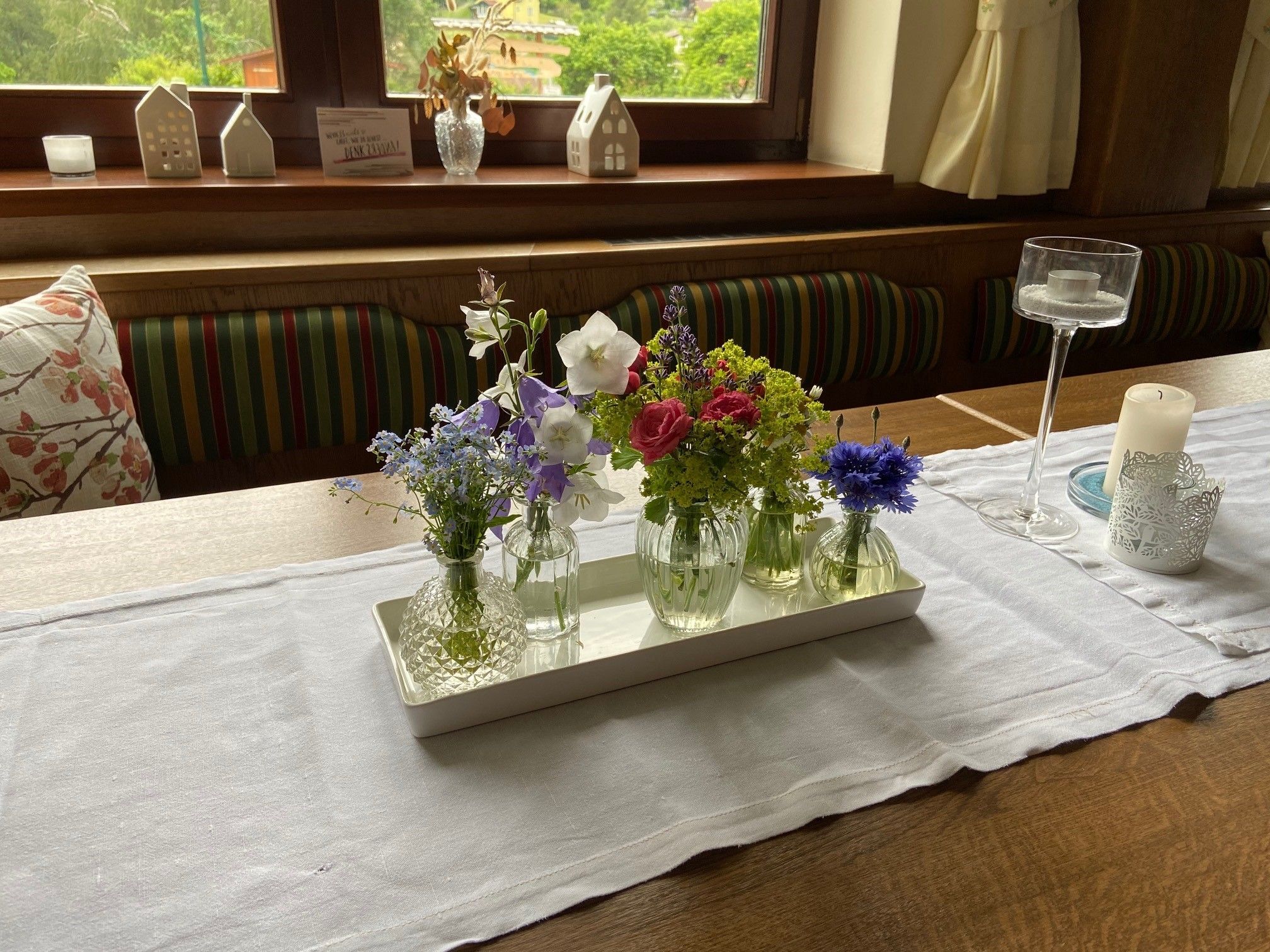 Ein Tisch mit einer weißen Tischdecke, dekoriert mit kleinen Vasen voller bunter Blumen und Kerzenhaltern.