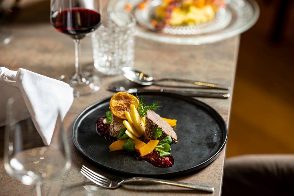 Gourmetgericht auf schwarzem Teller mit Rotwein im Hintergrund.