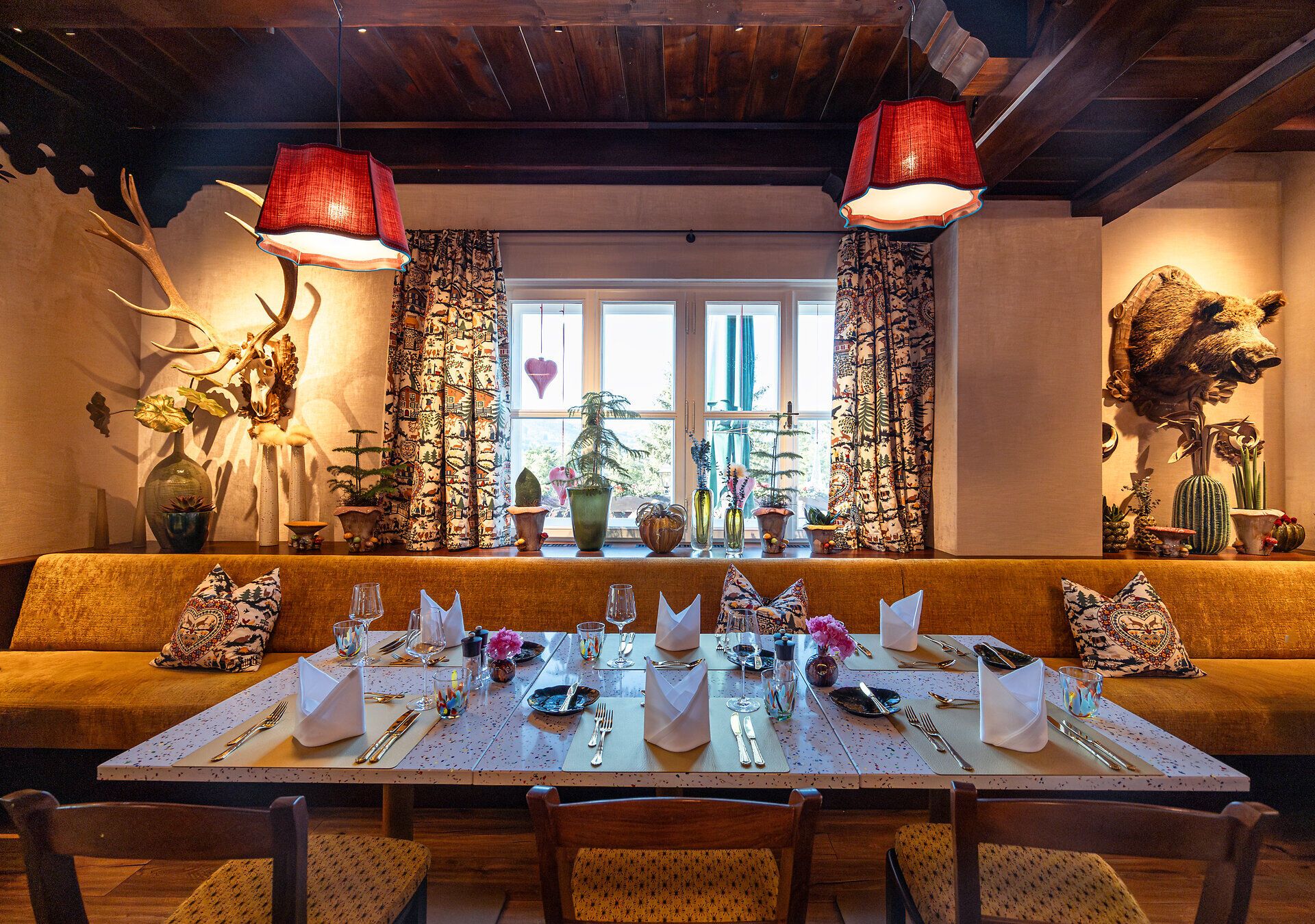 Gemütlicher Essbereich mit großen Fenstern, grünen Polstermöbeln und Pflanzen, mit Blick auf die Landschaft.