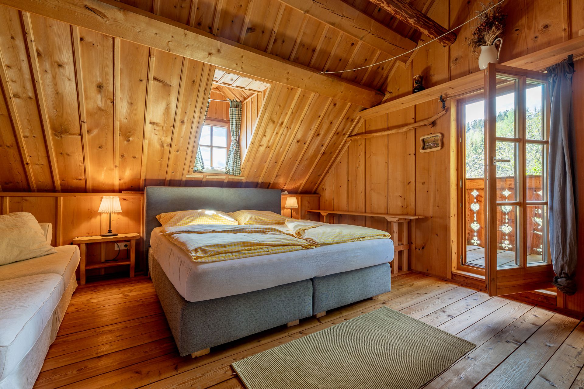 Schlafzimmer mit Holzvertäfelung, Doppelbett, Teppich und offener Tür zum Balkon.