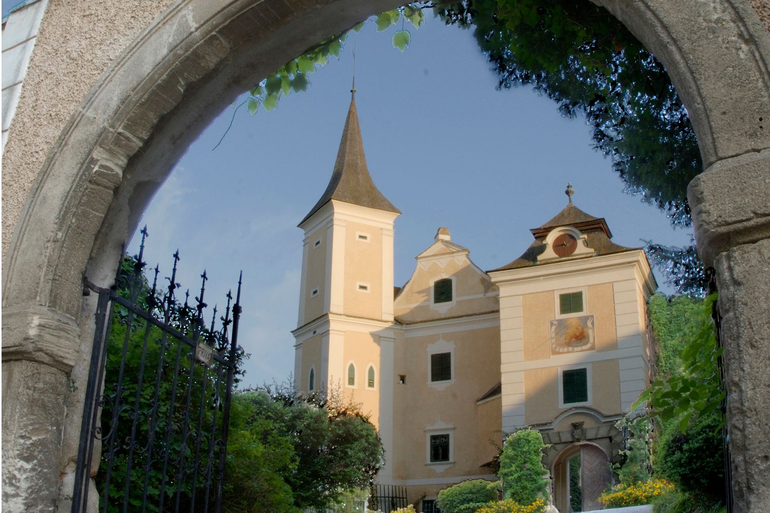 Schloss Mühlbach hinter einem steinernen Torbogen mit schmiedeeisernem Tor.