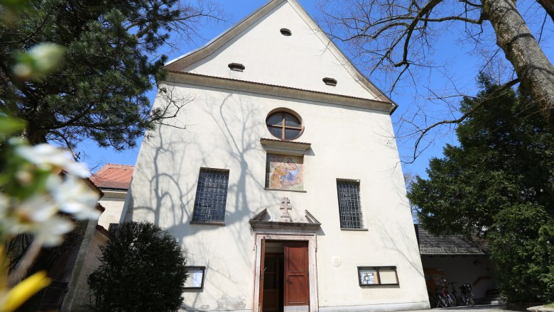 Fassade der Kapuzinerkirche mit Eingang und Fenstern, umgeben von Bäumen.