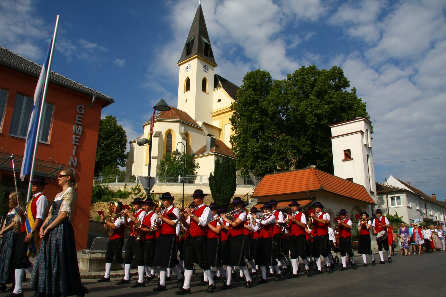 Eine Blaskapelle in traditioneller Kleidung marschiert vor einer Kirche.