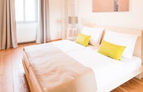 Helles Schlafzimmer mit Doppelbett, Holzboden und modernen Lampen.