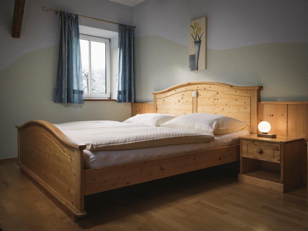 Ein Schlafzimmer mit einem Holzbett, Nachttisch und Lampe, blauen Vorhängen und einem Bild an der Wand.