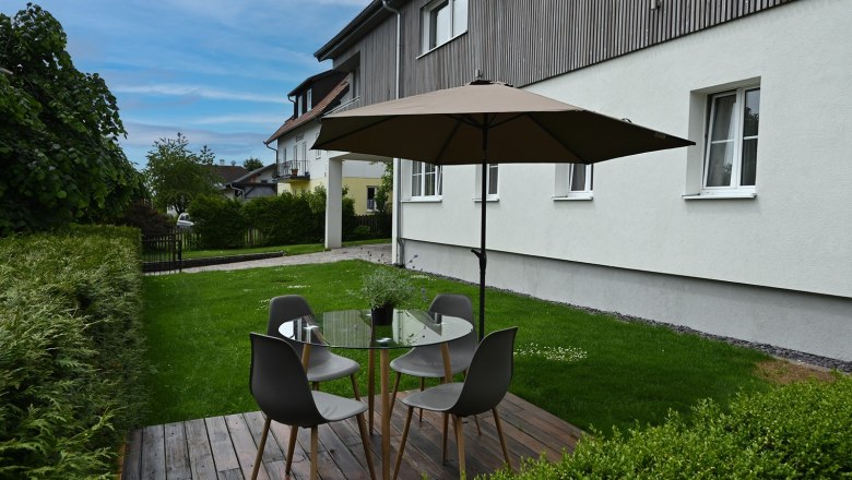 Garten mit Sitzbereich, Tisch, St&uuml;hlen und Sonnenschirm auf Holzterrasse.