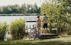 Zwei Personen gehen Richtung Bergwerksee entlang eines Stegs, ihre Räder haben sie vorher abgestellt