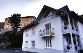 Zwei H&auml;user, eines wei&szlig; mit Balkon, das andere gelb, mit Dekoration.