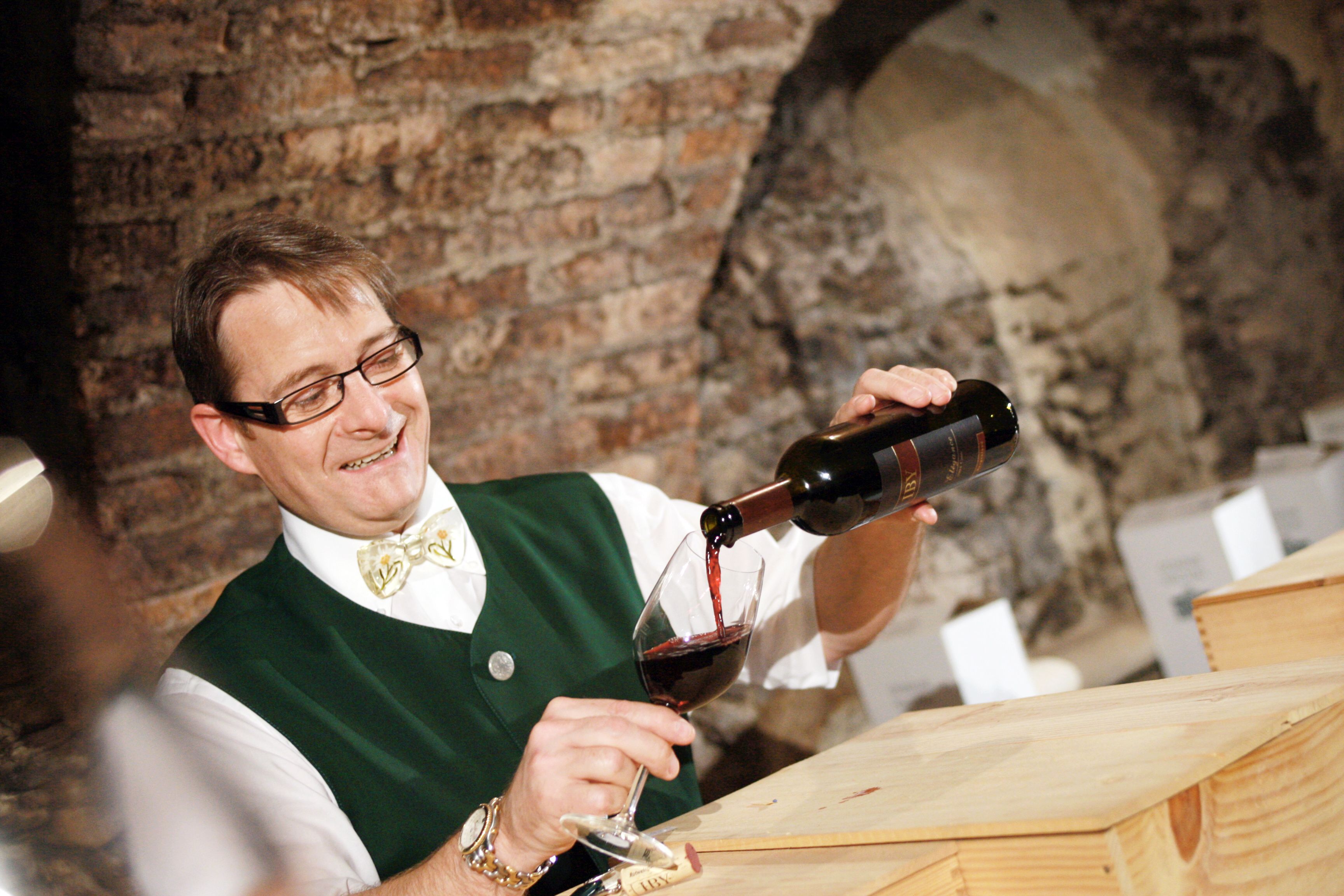 Ein Mann in traditioneller Kleidung schenkt Rotwein in ein Glas ein.