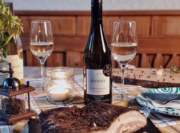 Tisch mit Weinflasche, zwei Gl&auml;sern, Kerze und Fleischgericht.