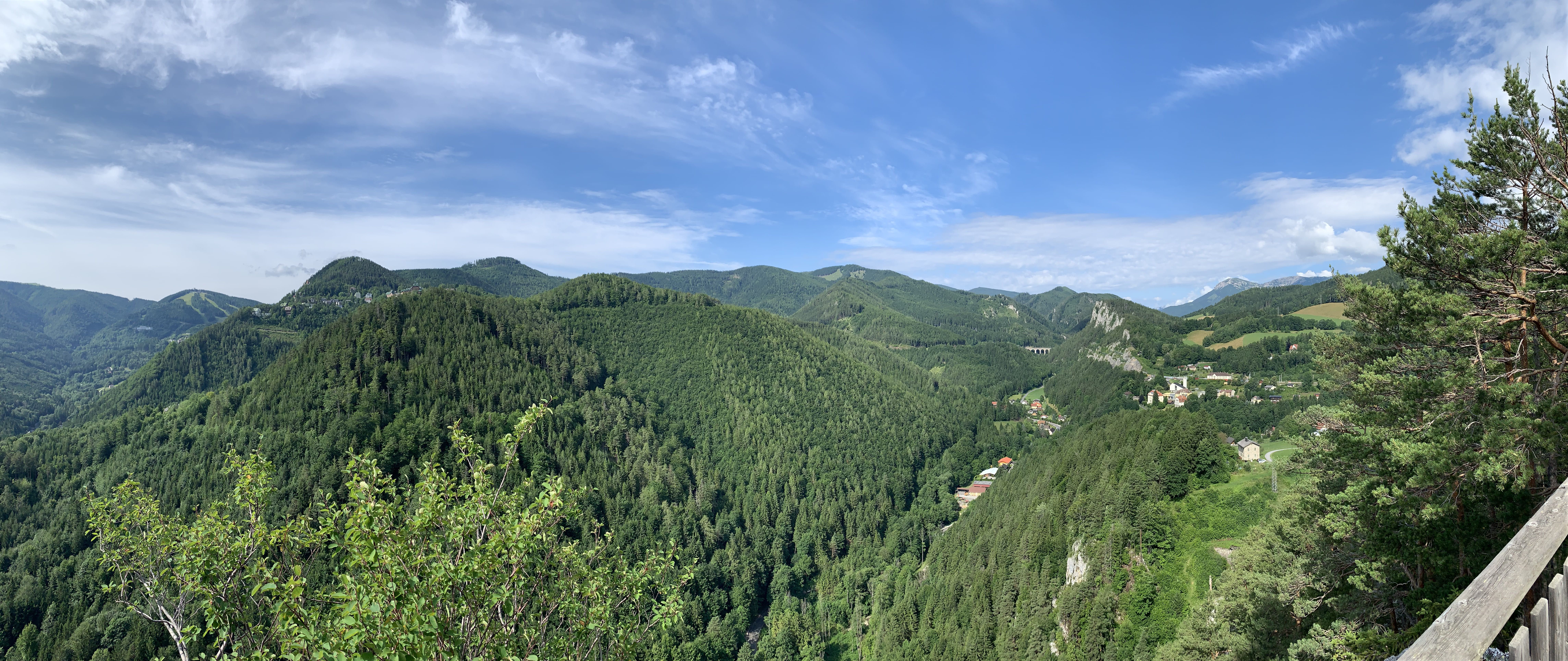 Panoramablick auf bewaldete Hügel und ein Tal mit verstreuten Häusern unter blauem Himmel.