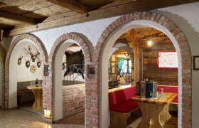 Rustikale Gaststube mit Holzmöbeln, Ziegelbögen und Jagdtrophäen an den Wänden.