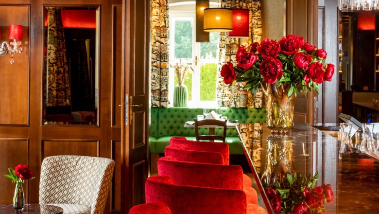 Elegantes Restaurant mit roten Samtstühlen, Kronleuchter und Blumendekoration.