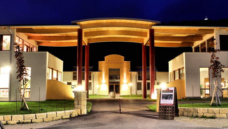 Beleuchtetes Geb&auml;ude des Weinguts Schlossberg bei Nacht.