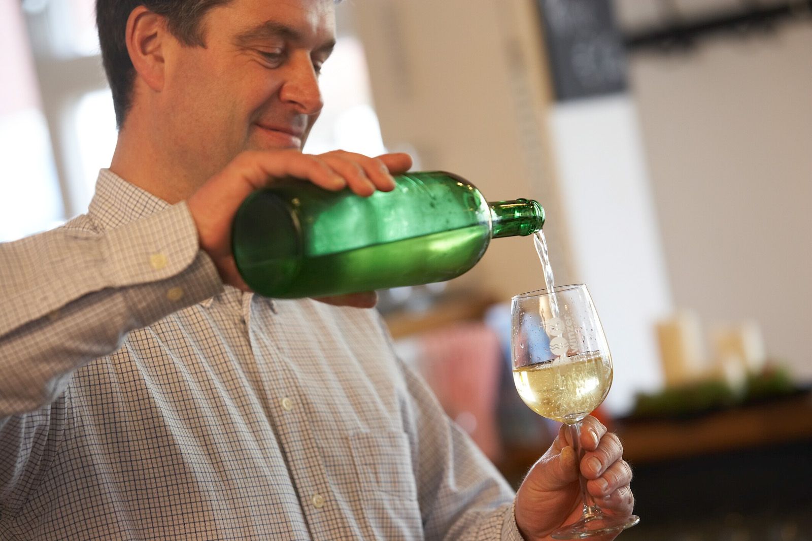 Ein Mann schenkt Weißwein aus einer grünen Flasche in ein Glas ein.