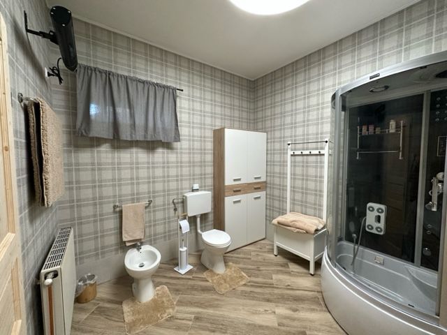 Modernes Badezimmer mit Duschkabine, Bidet, Toilette und Schrank auf Holzfußboden.