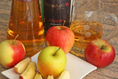 Verschiedene Apfelsorten und Apfelsaft auf einem Tisch.