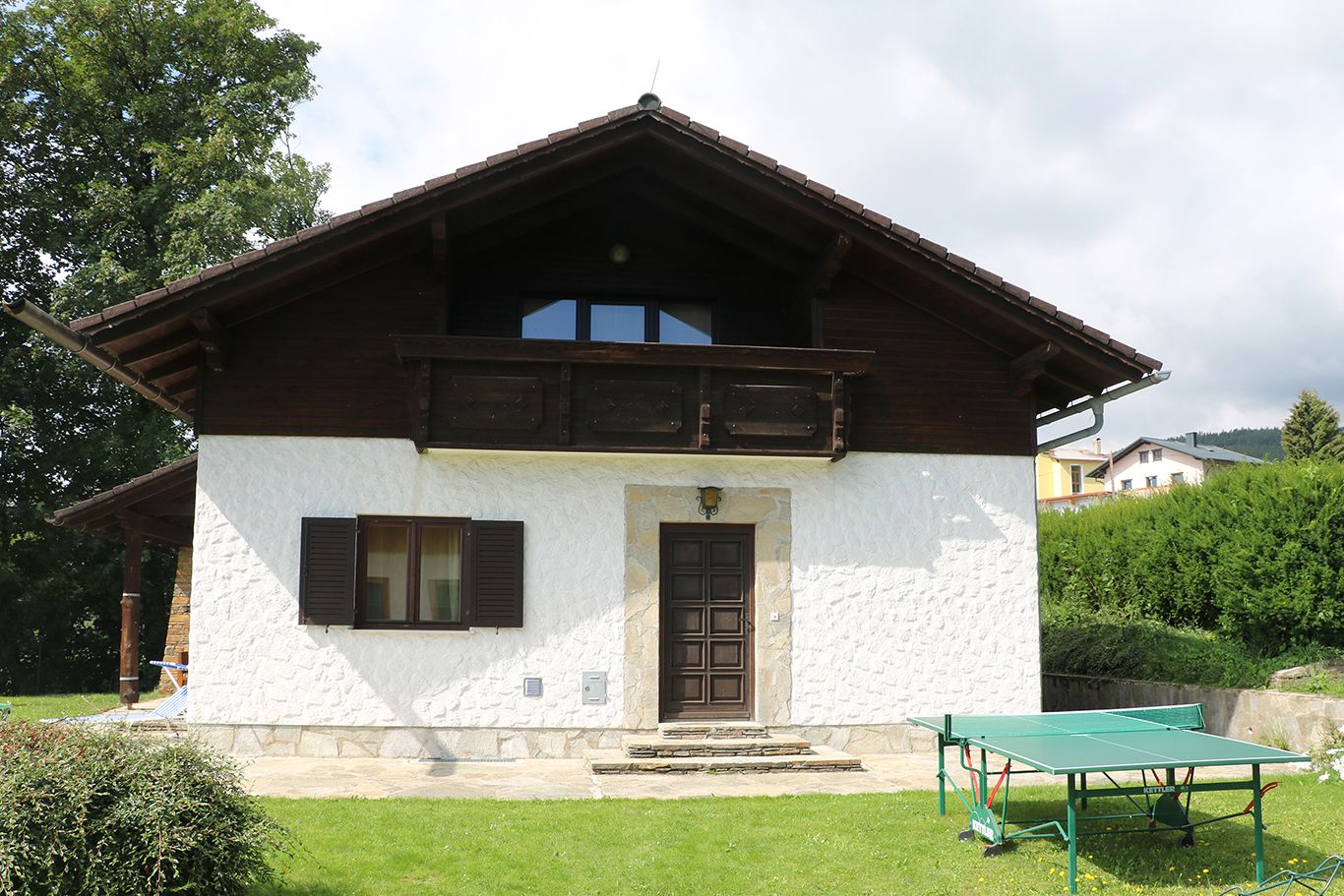 Ein weißes Haus mit Holzbalkon und Tischtennisplatte im Garten.