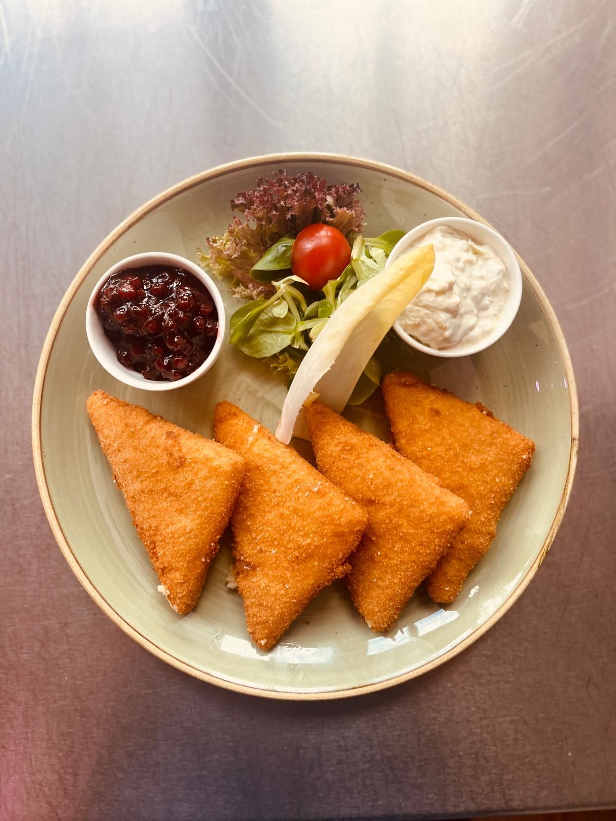 Ein Teller mit panierten Käse, Salat, Preiselbeeren und einer weißen Soße.