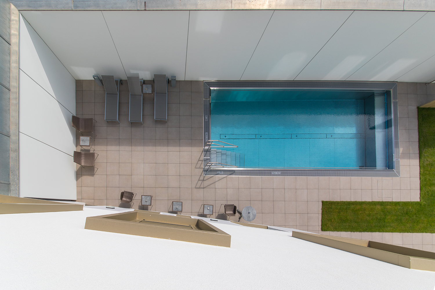 Draufsicht auf einen rechteckigen Pool mit Liegestühlen und Tischen auf einer gefliesten Terrasse.