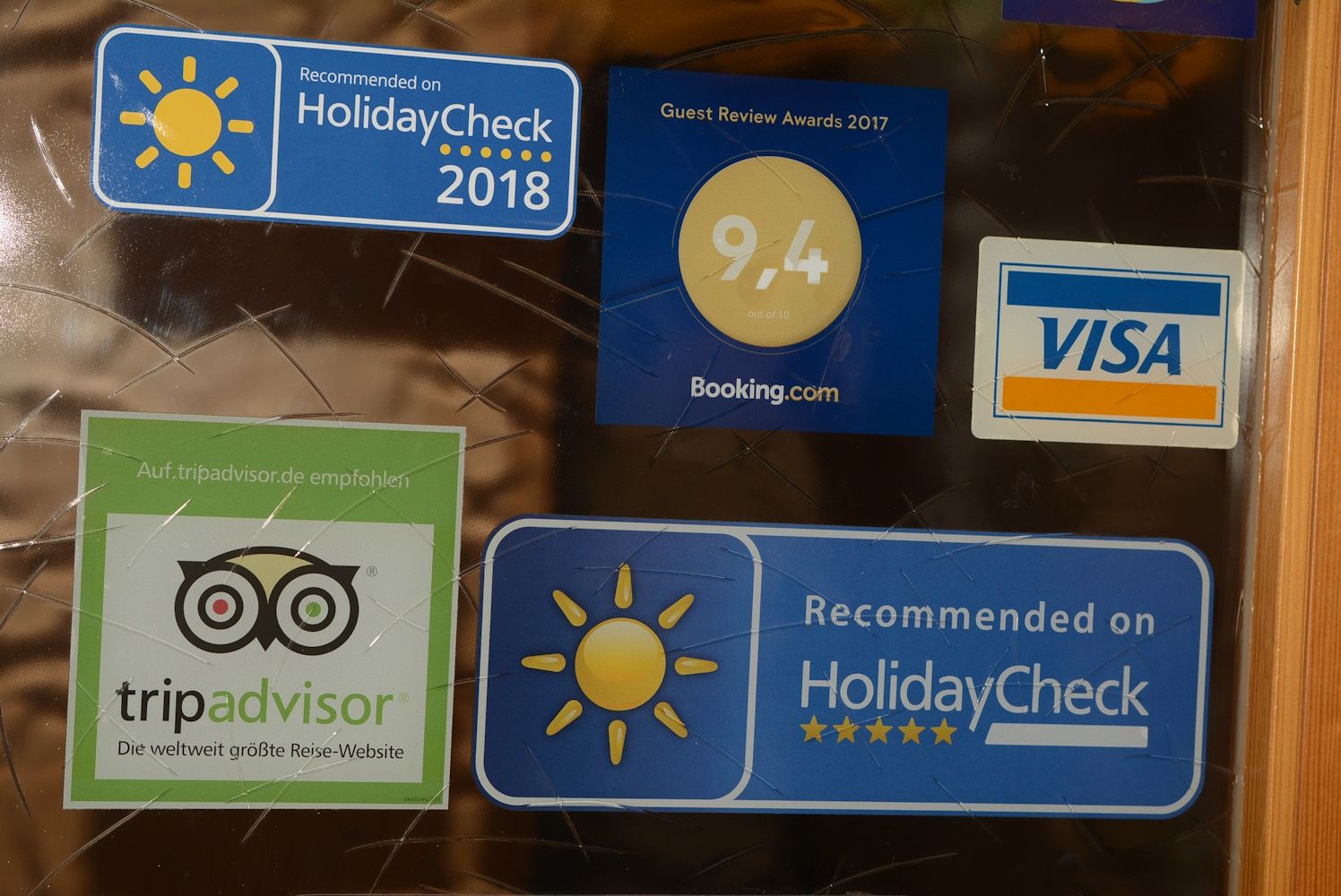 Aufkleber von HolidayCheck, Booking.com, TripAdvisor und Visa auf einer Glasoberfläche.
