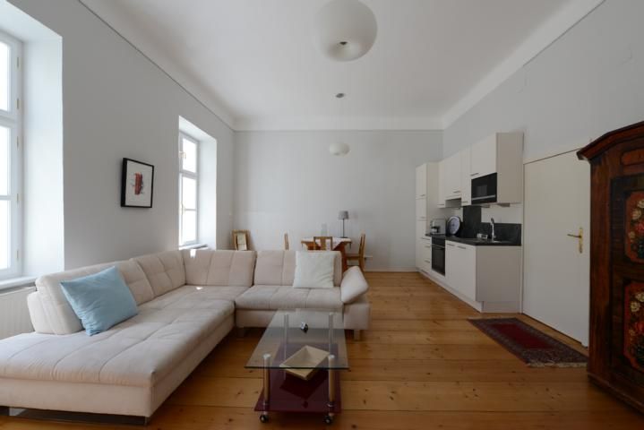 Helles Wohnzimmer mit Ecksofa, Glastisch, Esstisch und Küchenzeile.