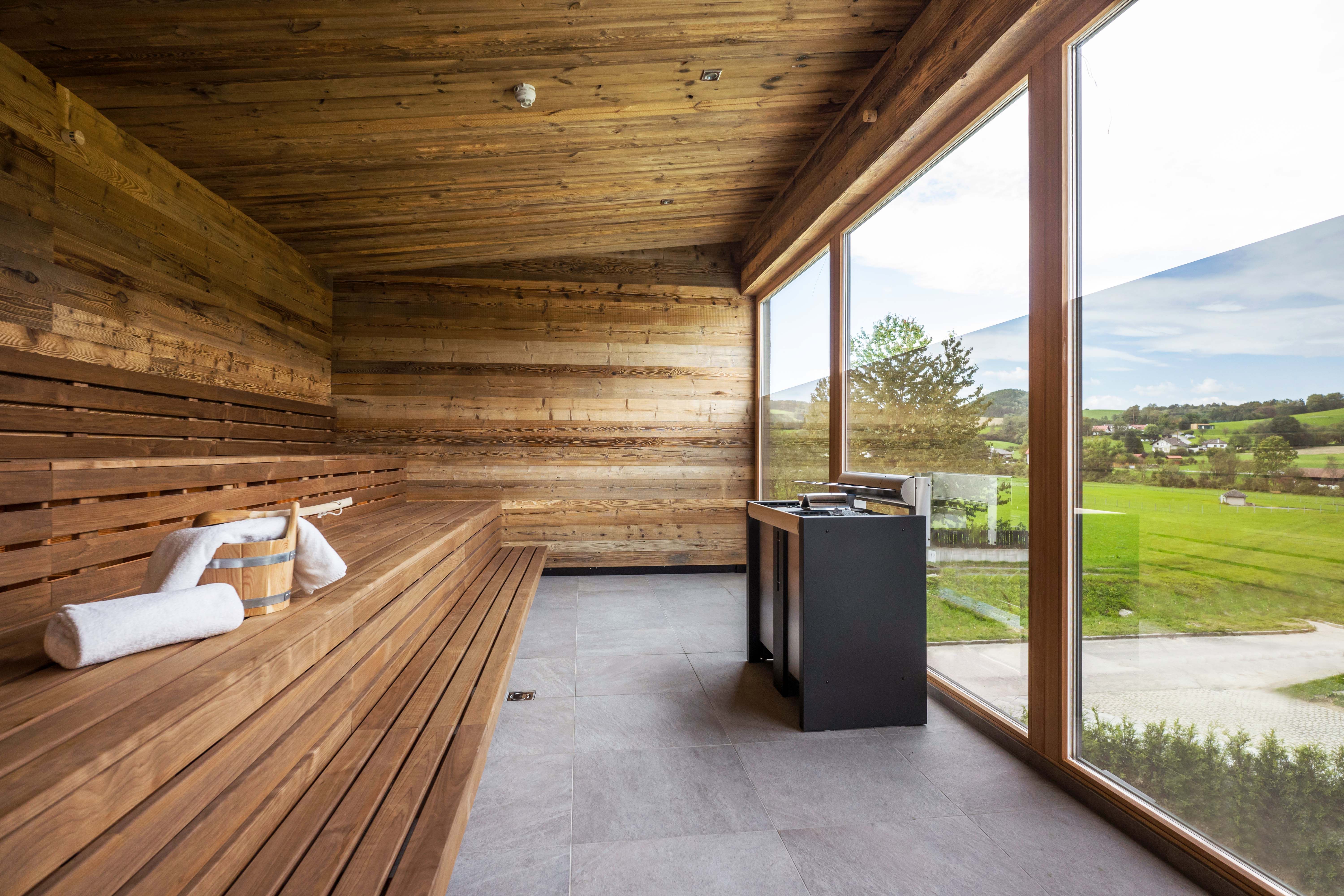 Innenansicht einer Sauna mit Holzwänden und -bänken, großem Fenster mit Blick auf grüne Landschaft.