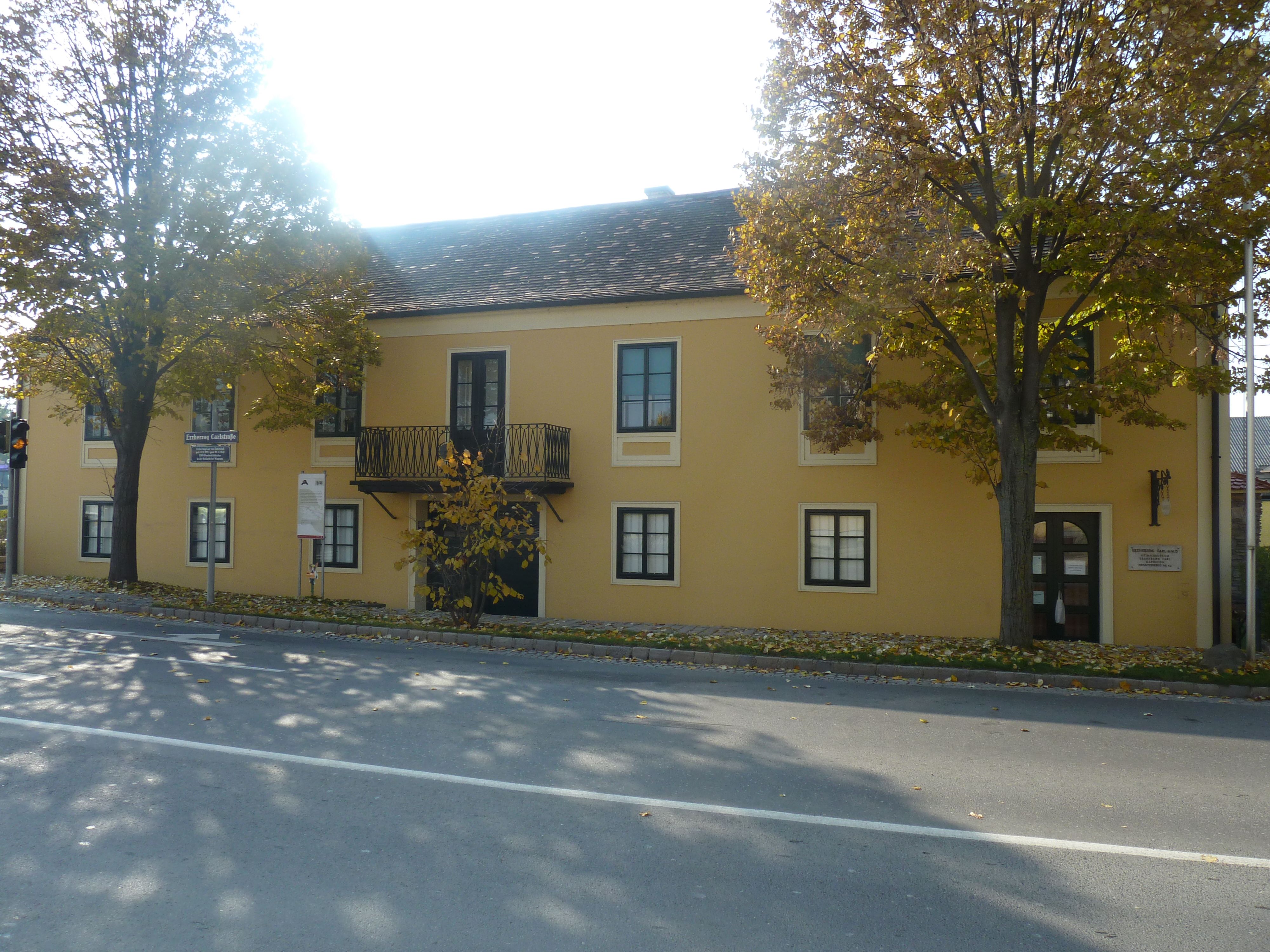 Gelbes Gebäude mit Balkon und Bäumen davor, Erzherzog Carl Haus und Napoleonmuseum in Deutsch-Wagram.