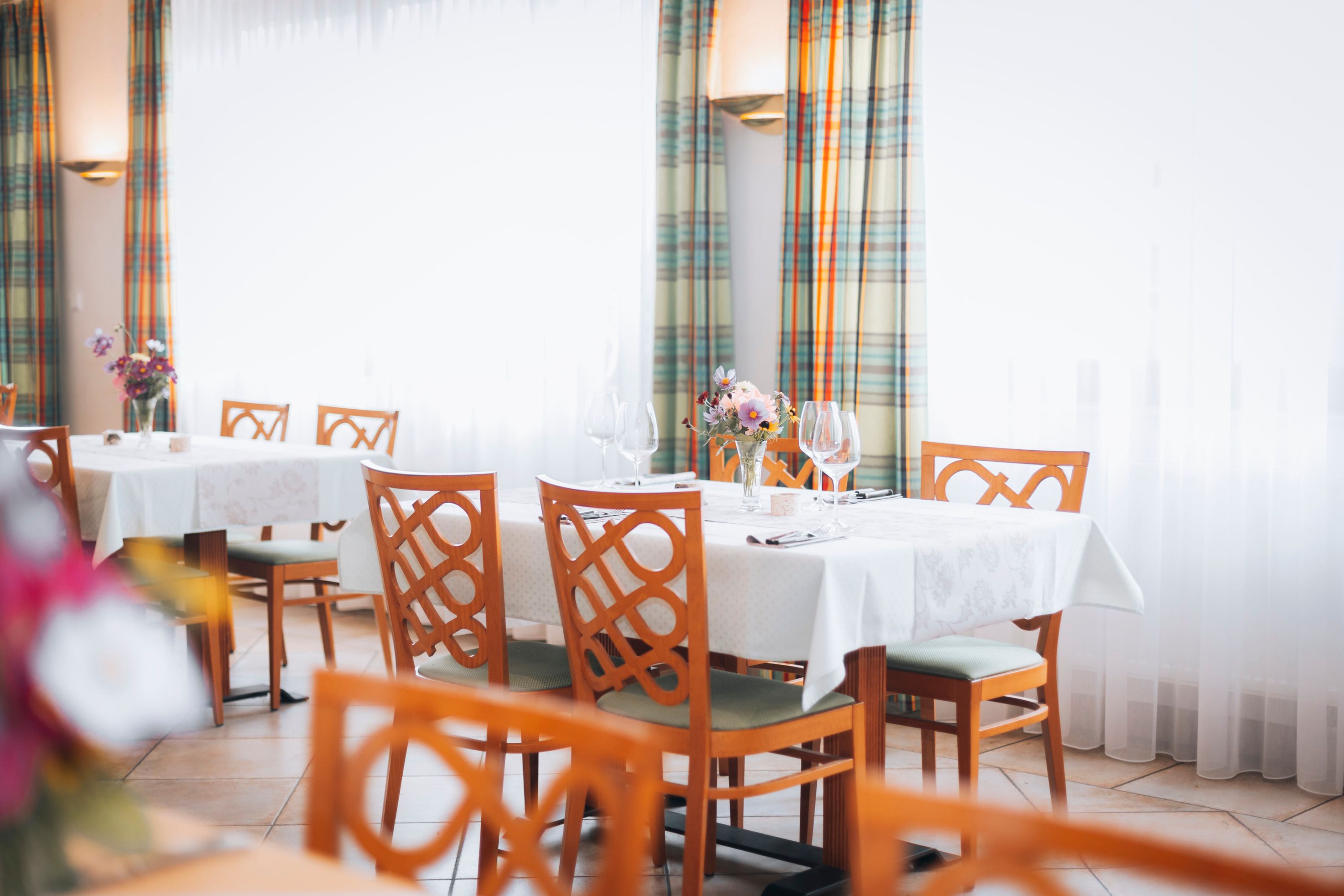 Elegantes Restaurant mit gedeckten Tischen, Blumenarrangements und Weingläsern.