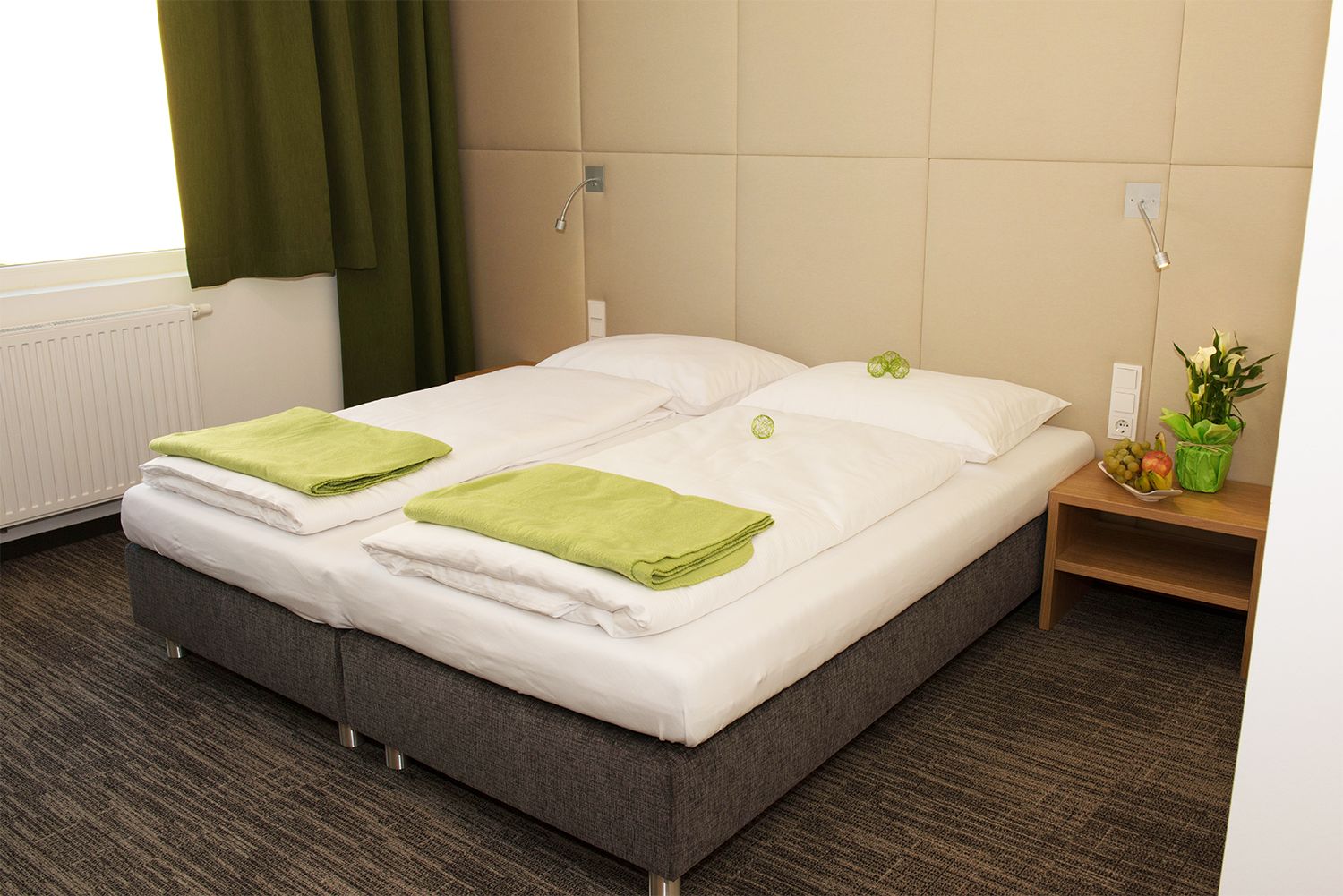 Gemütliches Hotelzimmer mit Doppelbett, grünen Handtüchern und Nachttisch mit Blumen und Obst.