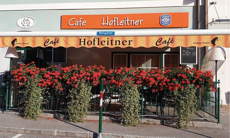 Außenansicht des Café Hofleitner mit roten Blumen und Markise.