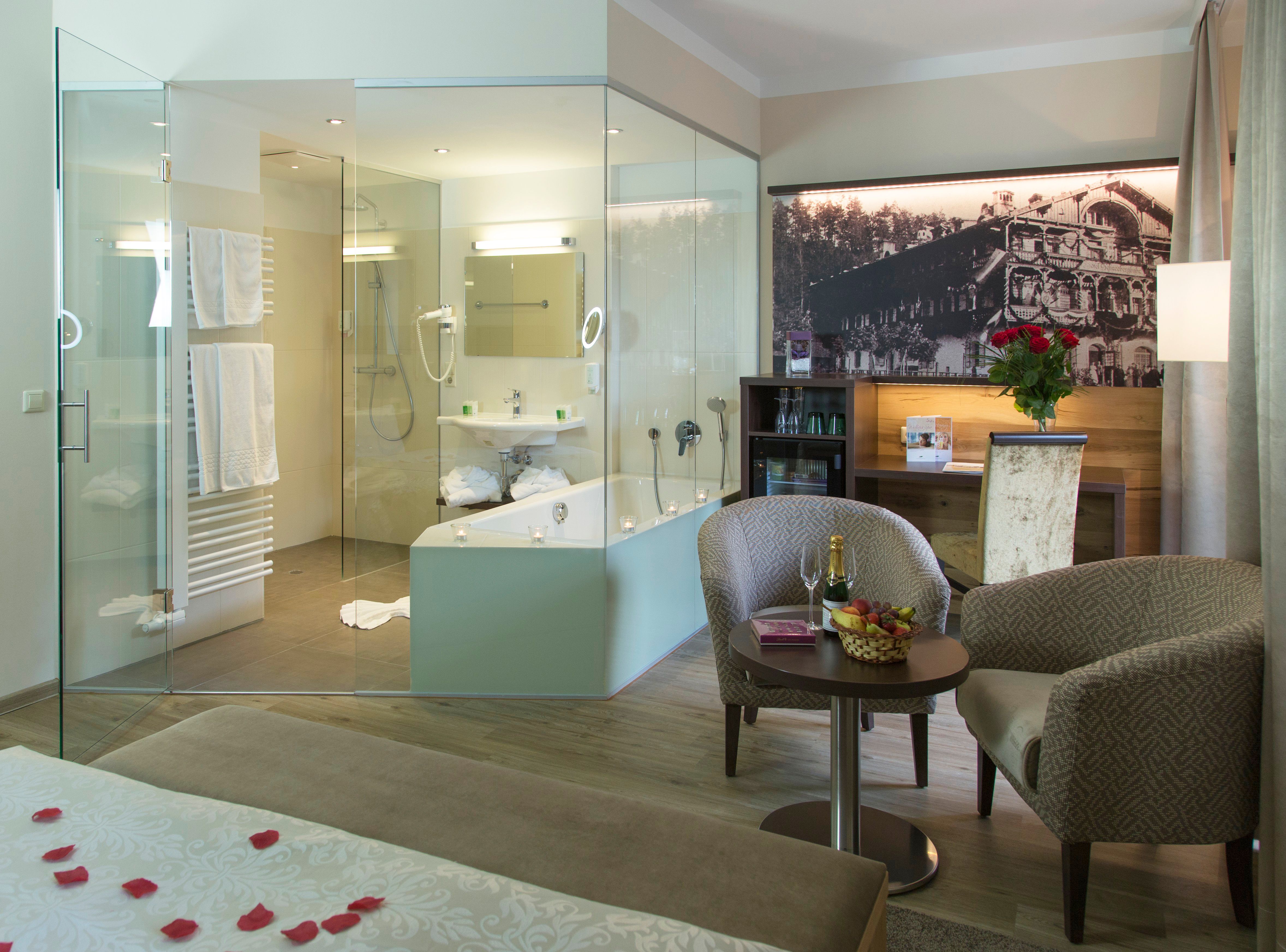 Hotelzimmer mit Bad und Sitzgruppe, dekoriert mit Rosen und Sekt.