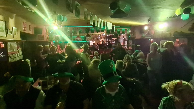 Menschen feiern in einem Pub mit grüner Dekoration und Hüten an St. Patrick's Day.