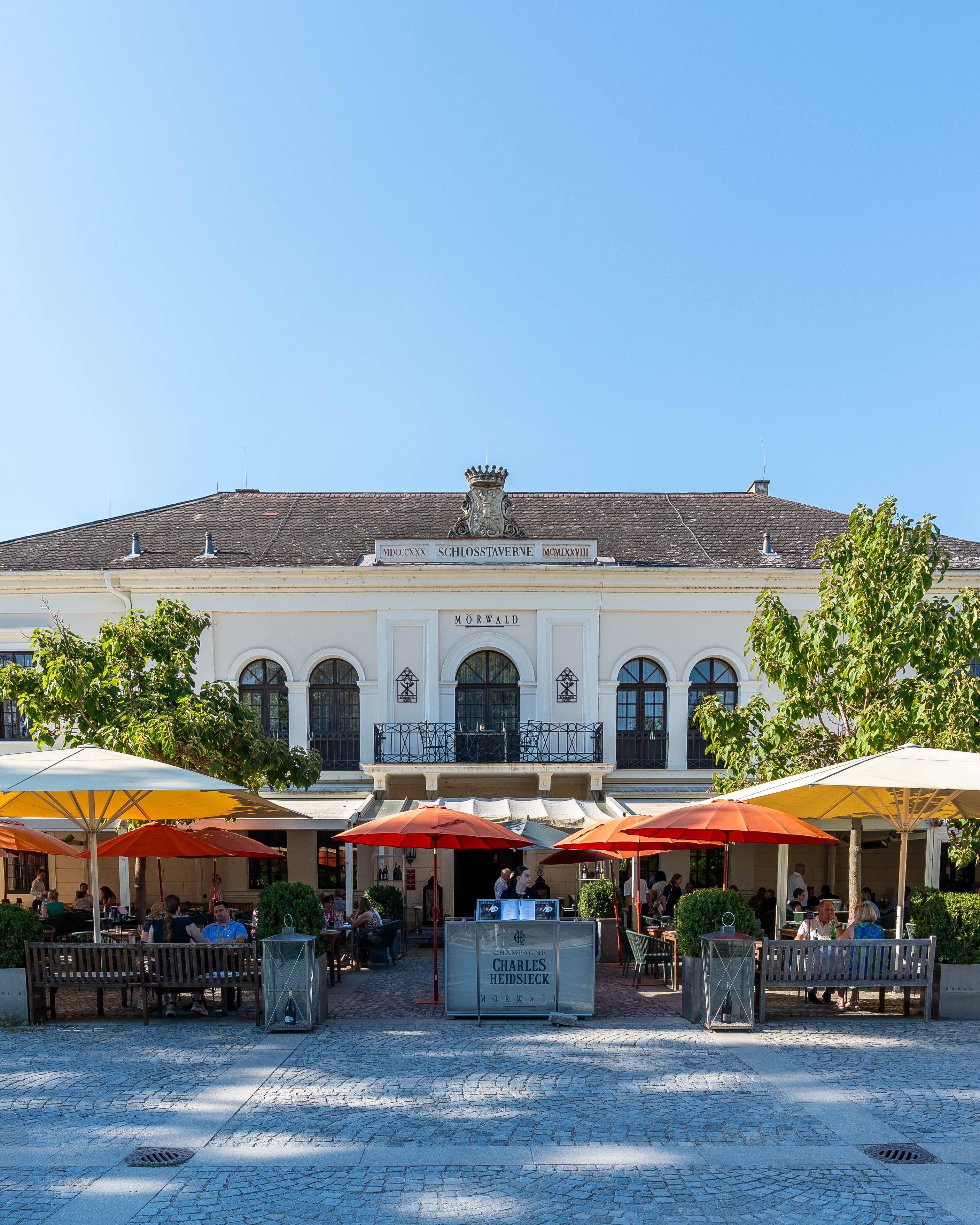 Frontansicht des Grafenegg Hotel & Restaurant mit Terrasse, Sonnenschirmen und Gästen vor dem Gebäude Mörwald in Grafenegg.