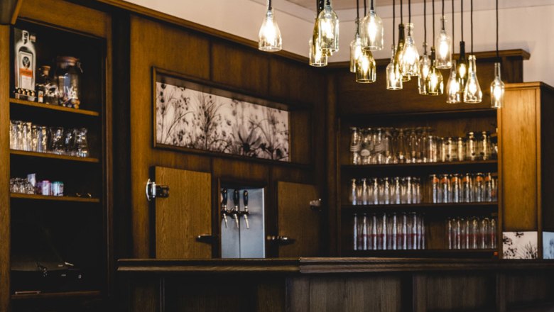 Eine gem&uuml;tliche Bar mit h&ouml;lzernem Interieur und h&auml;ngenden Flaschenlampen.