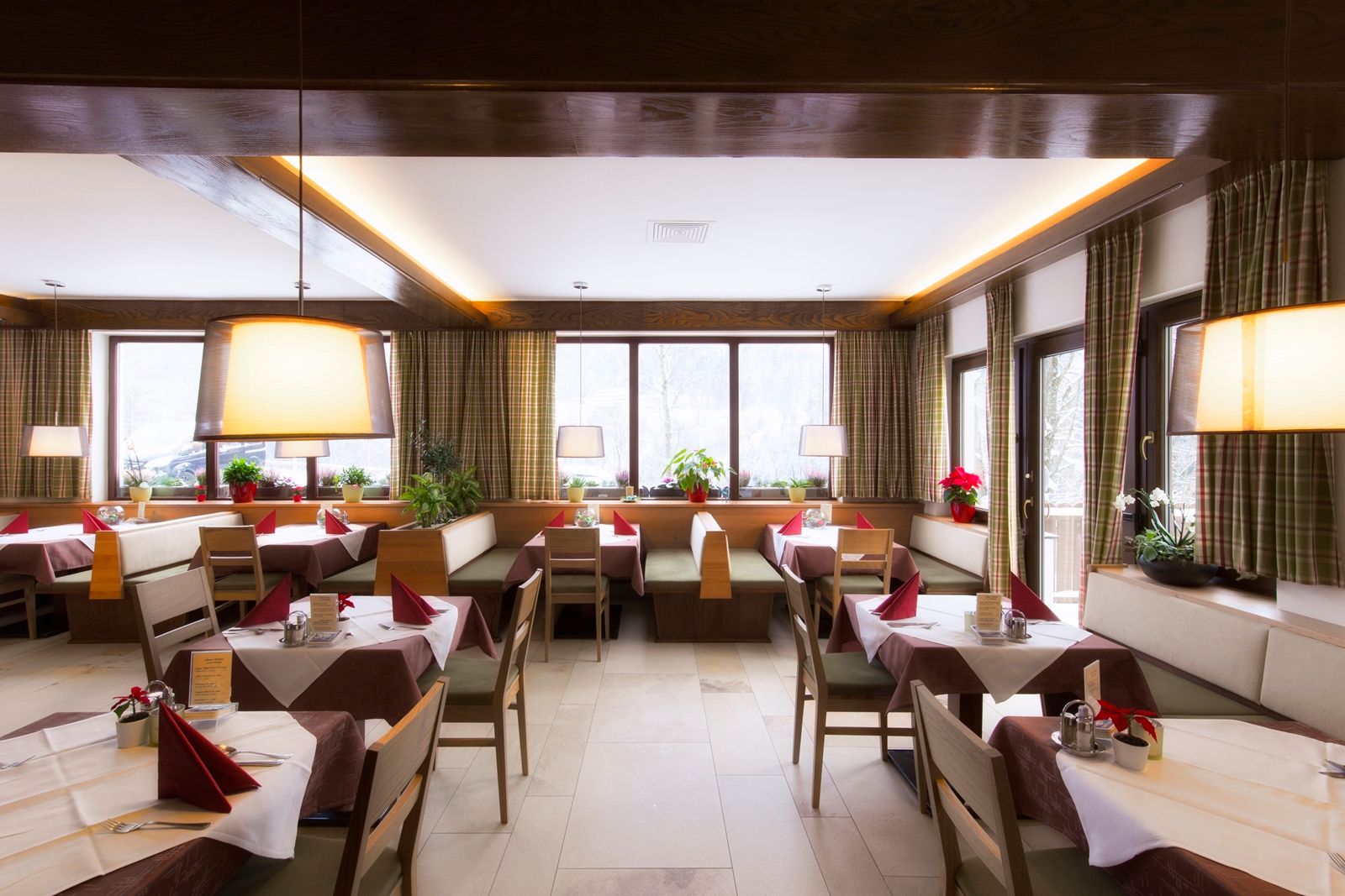 Innenansicht eines gemütlichen Restaurants mit Holzmöbeln, gedeckten Tischen und großen Fenstern.