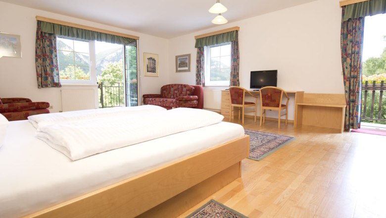 Doppelzimmer mit Holzboden und roter Couch sowie bunten Vorh&auml;ngen